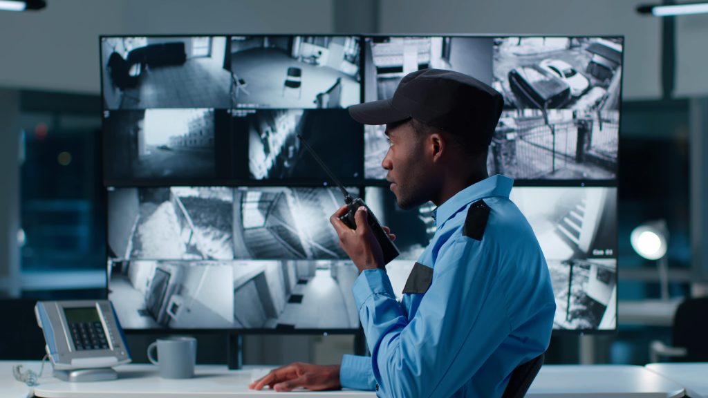 African-American security officer watching the screens talking on radio in control room