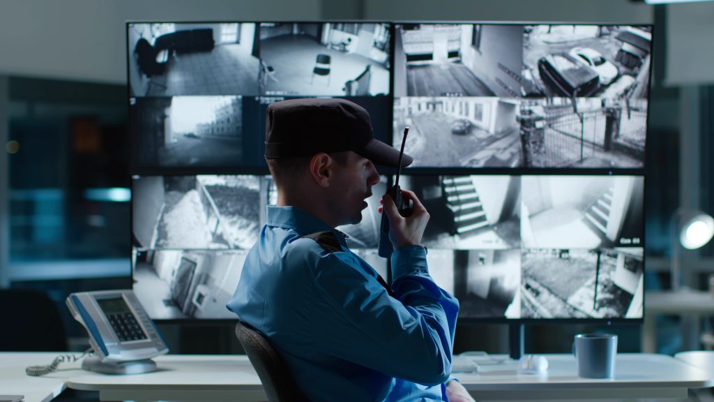 Security guard talking on walkie talkie while looking at cctv camera footage on multiple computer screen