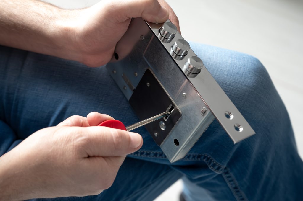 The locksmith using a screwdriver to adjust a metal door lock mechanism, demonstrating a close-up of the locksmithing process and repair work with attention to detail