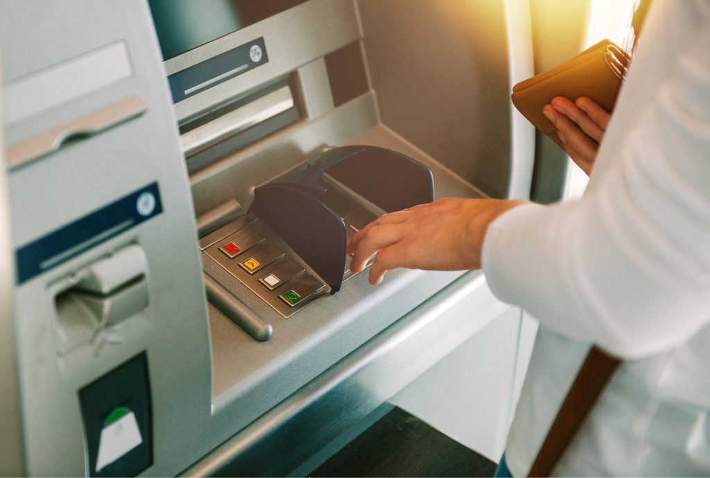 Woman using ATM holding wallet an pressing the PIN security number on the keyboard automatic teller machine